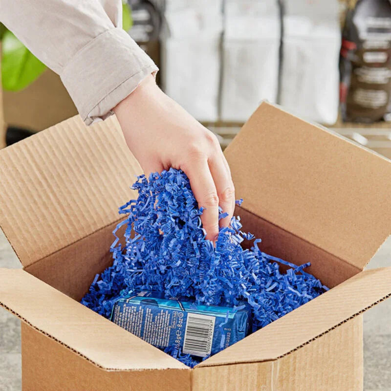 Hand placing vibrant Crinkle paper shreds - Royal Blue inside a cardboard box as protective packaging filler