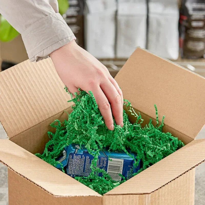Hand placing eco-friendly green paper filler in cardboard shipping box, Greenii packaging