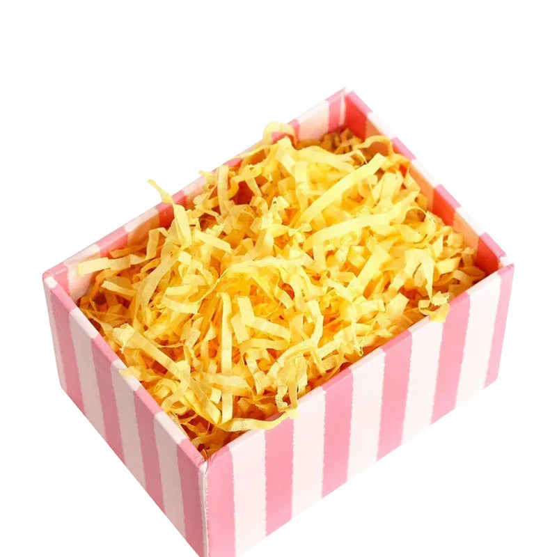 Yellow shredded paper packaging filler in a pink striped box for eco-friendly gift packaging
