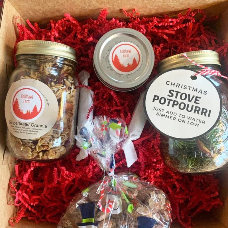 Gift box with Goldhawk Farm gingerbread granola jar, Christmas stove potpourri, and festive treats on red shredded filler, eco-friendly packaging.